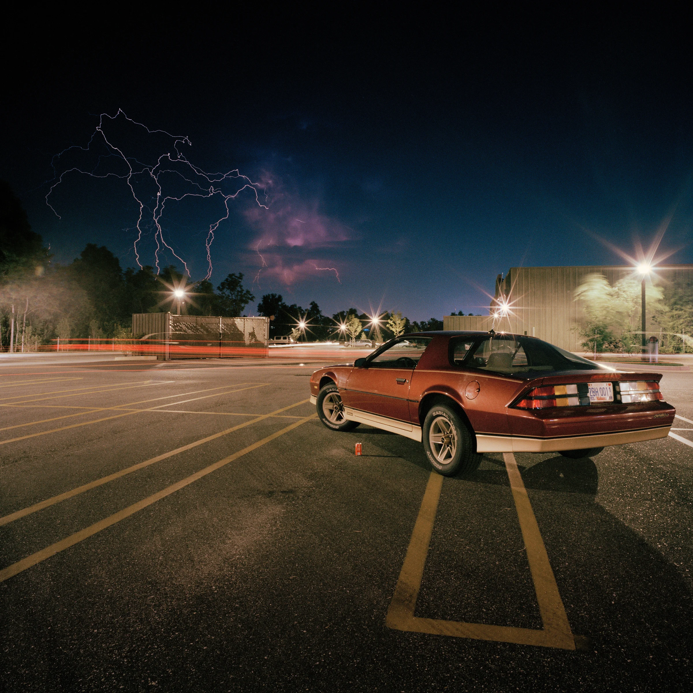 Lightning in a night sky above a parked car in Giovanni Chiaramonte’s photograph Mobile, Alabama.